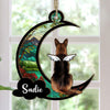 A personalized suncatcher ornament in the shape of a crescent moon with a picture of a dog breed and the name 'Sadie' printed on it. The ornament is hanging by a string and appears to be placed in front of a light source, creating a colorful reflection.