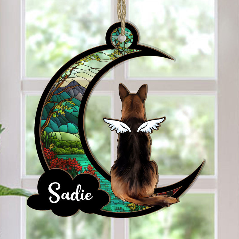 A personalized suncatcher ornament in the shape of a crescent moon with a picture of a dog breed and the name 'Sadie' printed on it. The ornament is hanging by a string and appears to be placed in front of a light source, creating a colorful reflection.