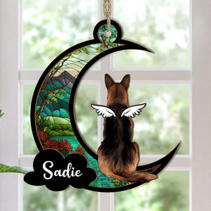 A personalized suncatcher ornament in the shape of a crescent moon with a picture of a dog breed and the name 'Sadie' printed on it. The ornament is hanging by a string and appears to be placed in front of a light source, creating a colorful reflection.