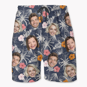 A pair of personalized beach shorts featuring a Hawaiian pattern with various faces and floral prints on a navy background.