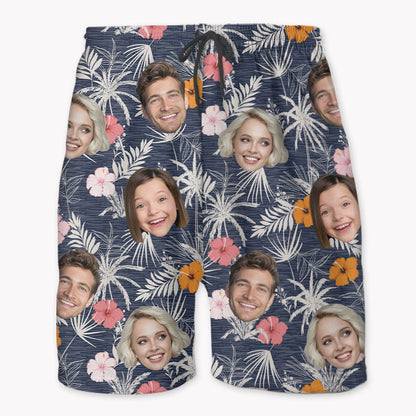 A pair of personalized beach shorts featuring a Hawaiian pattern with various faces and floral prints on a navy background.